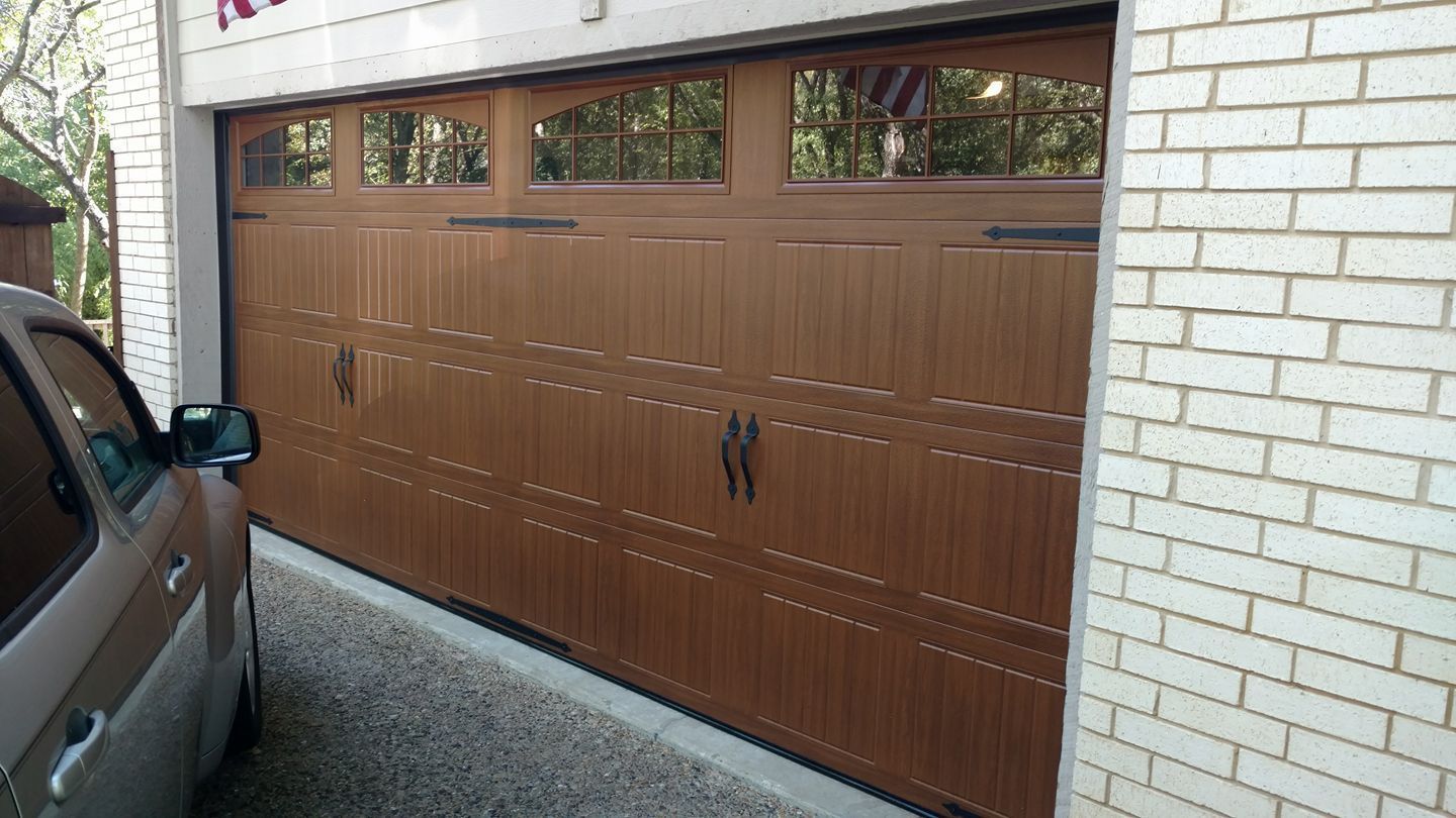 Brown garage door with windows on a white brick house, with part of a car visible at left.