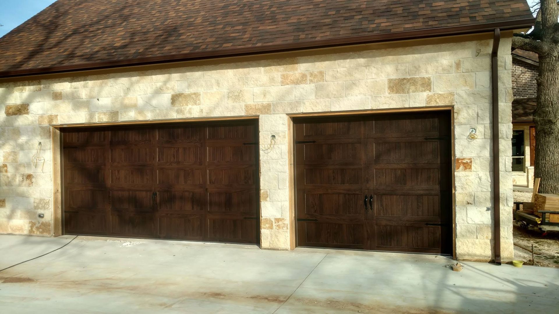 Stone garage with two large brown wooden doors on a sloped driveway
