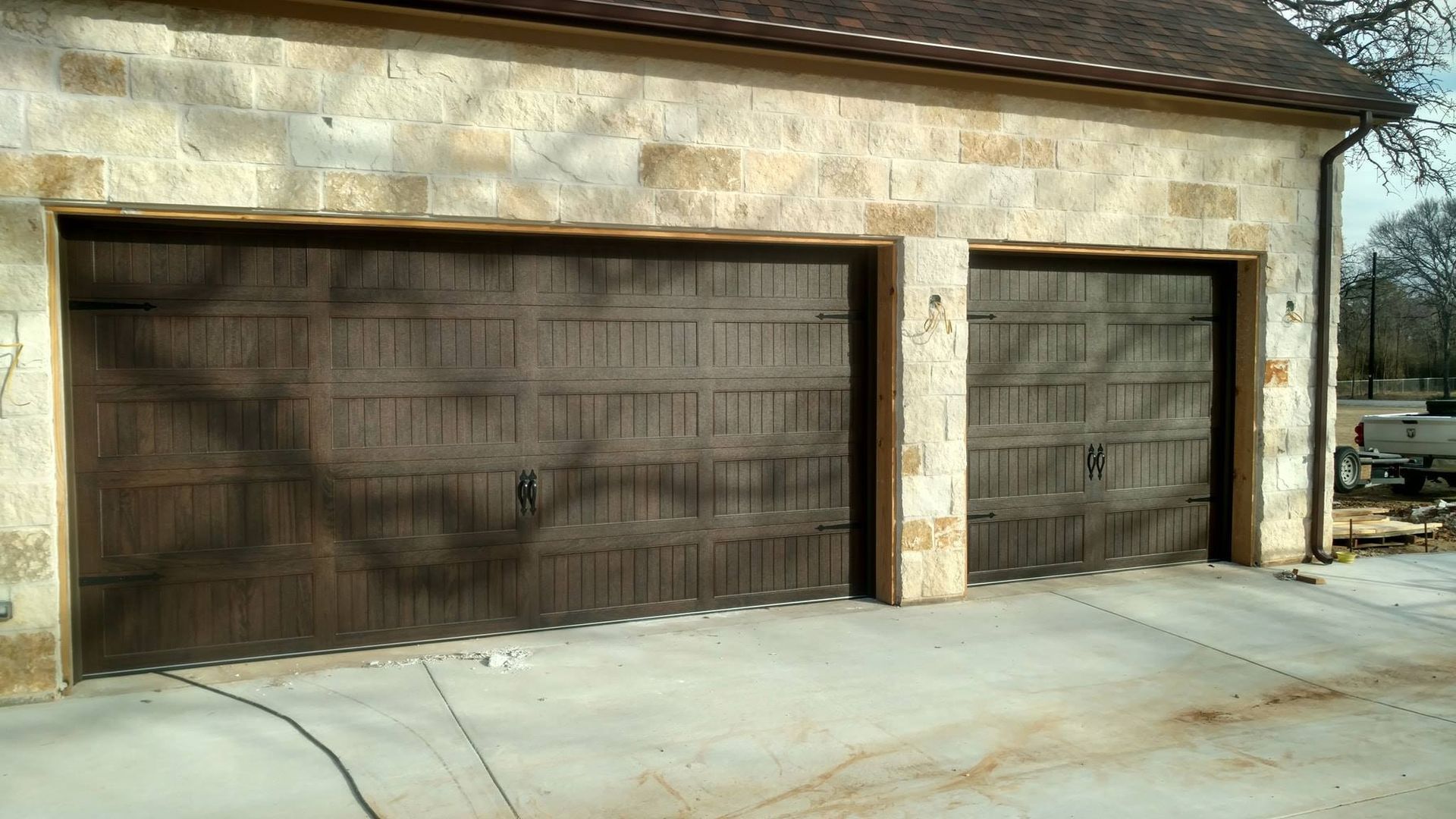 Two brown wooden garage doors on a stucco house exterior with a concrete driveway
