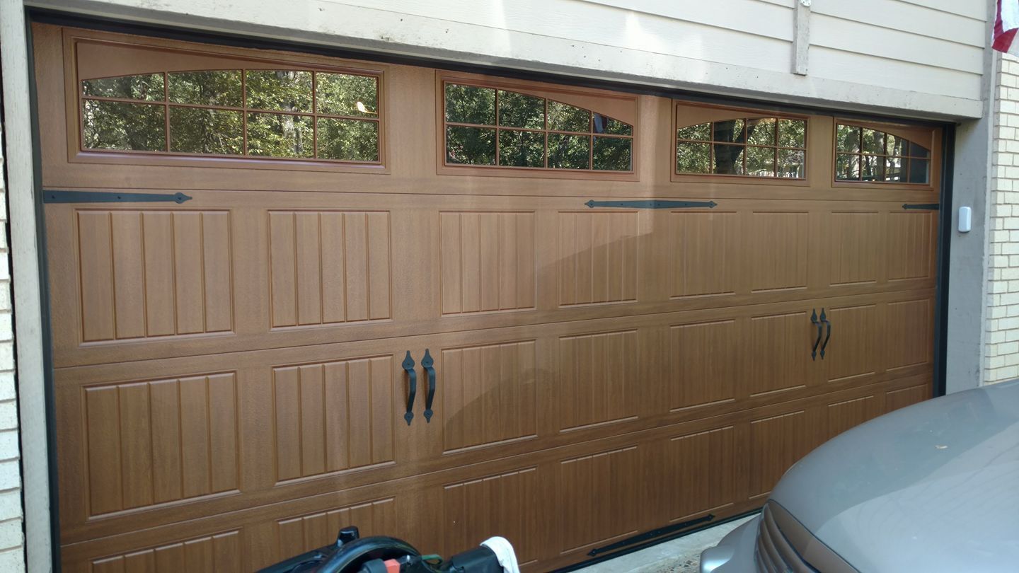 Brown wooden garage door with windows along the top, viewed from outside beside a parked car.