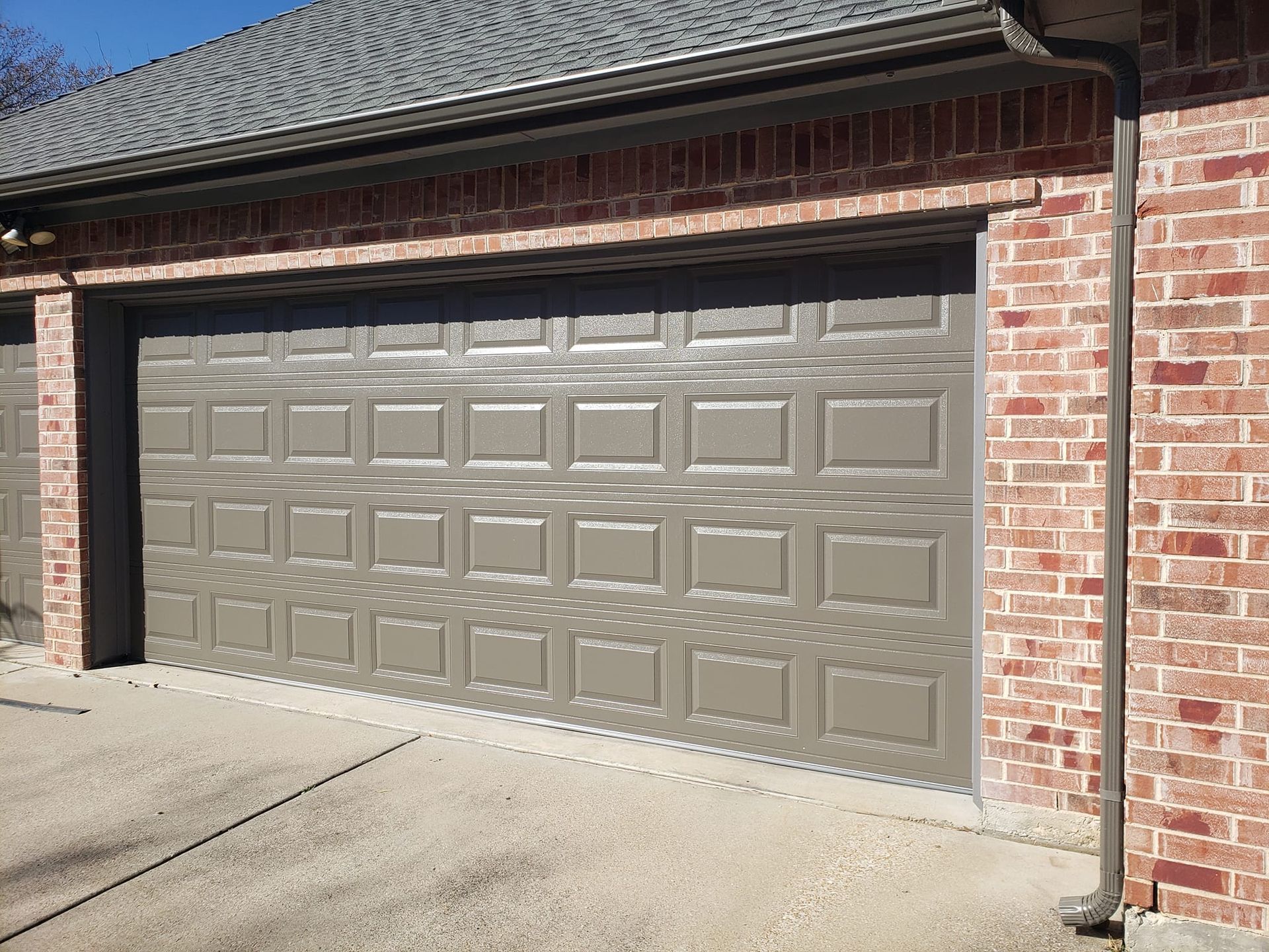 Closed beige garage door on a brick house with a concrete driveway.
