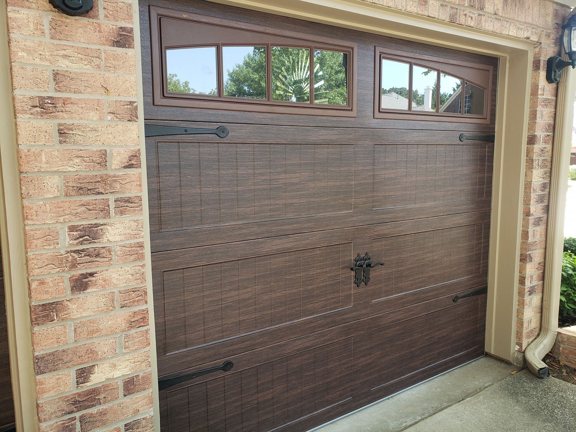 Brown garage door with small upper windows on a brick house exterior