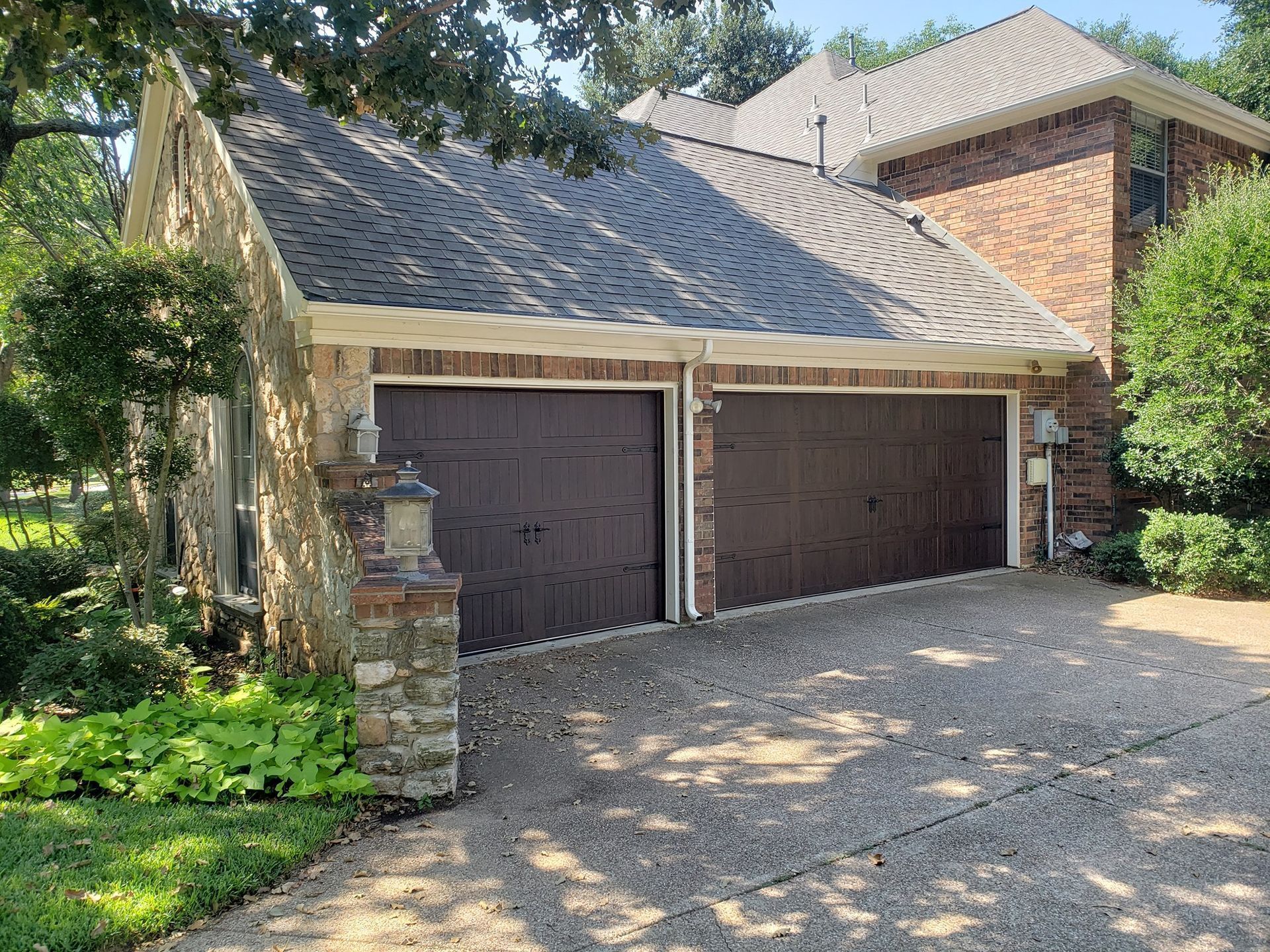Brick house with a two-car garage, dark wooden doors, and a gravel driveway under trees