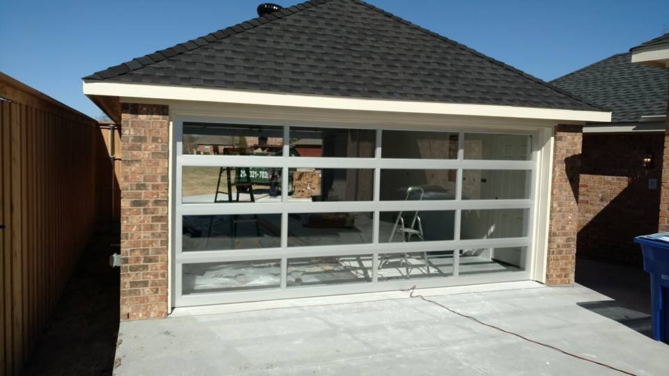 Single-car garage with a white glass-paneled door and brick trim in a driveway under a clear sky
