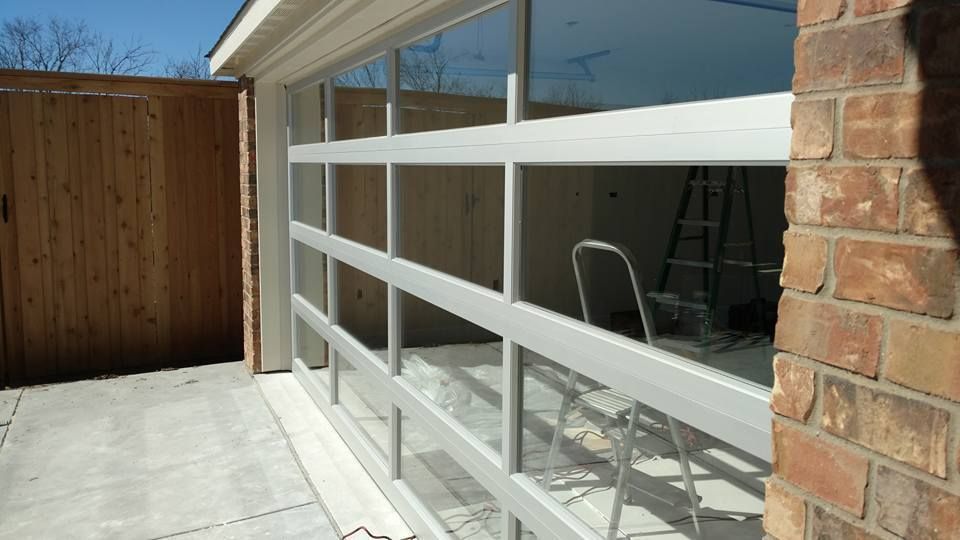 House patio with large reflective windows, white railing, brick wall, and a wooden fence.