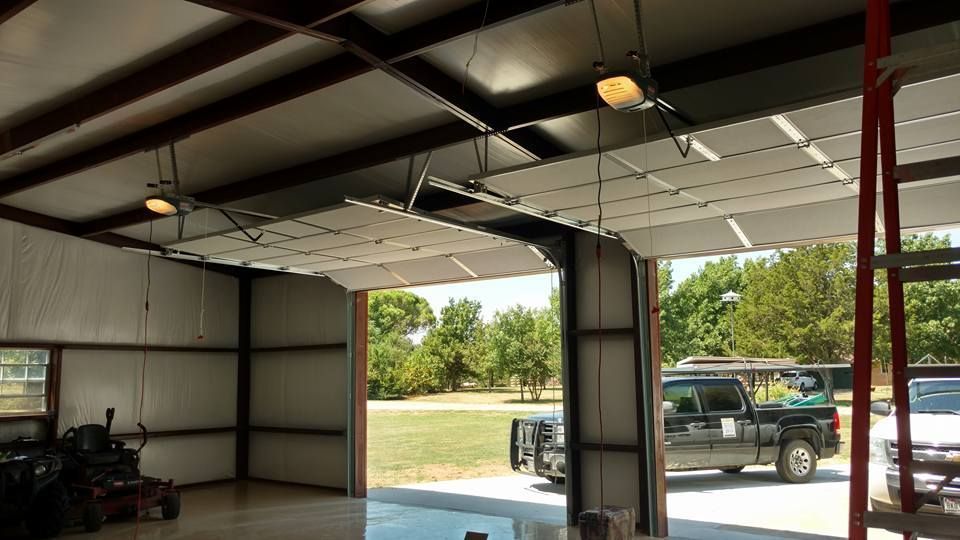 Inside a garage with open door, a black pickup truck is parked outside on a sunny day.