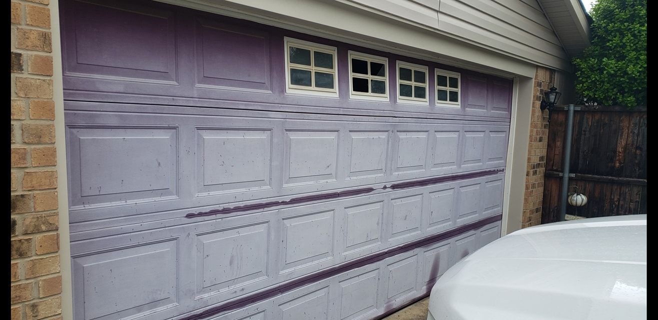 White garage door with small windows on a house exterior, viewed beside a car in a driveway