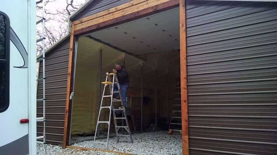 Person on ladder working inside a garage with the door open, framed by wood and dark siding.