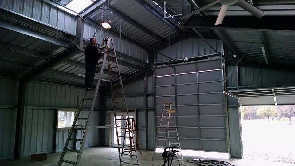 Person on a ladder working inside a large metal shed with an open doorway.