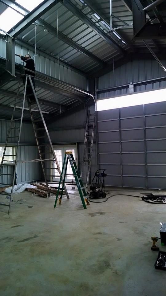 Empty industrial warehouse with a ladder, scaffold, and construction equipment under a high metal roof.
