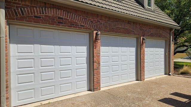 Three white garage doors on a brick house with a sloped shingle roof and driveway.