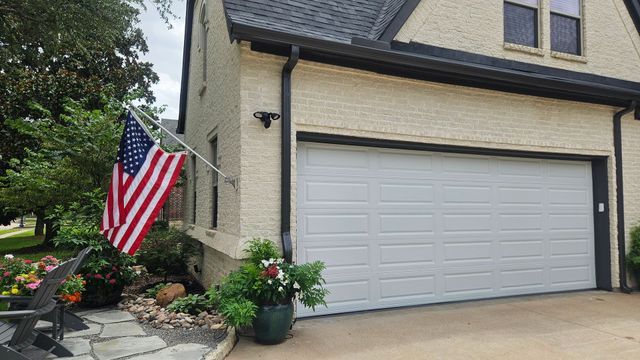 Suburban home exterior with two-car garage, American flag, and flower pots by the entrance