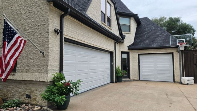 House exterior with two white garage doors, an American flag, and a basketball hoop in the driveway