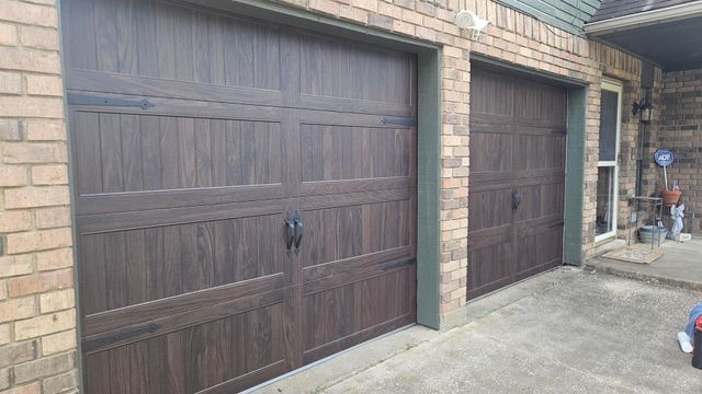 Two brown garage doors on a brick house, with a concrete driveway and side entrance.