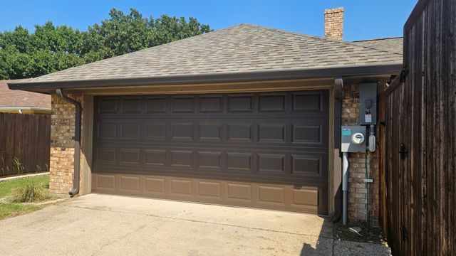 Suburban house with a two-car garage and tan driveway under a clear blue sky