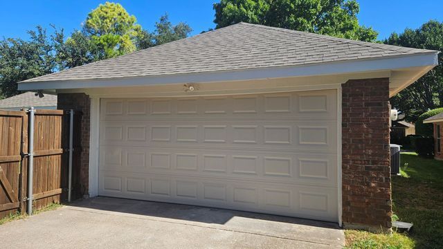 Detached two-car garage with beige door, brick side wall, and wooden fence on a sunny day