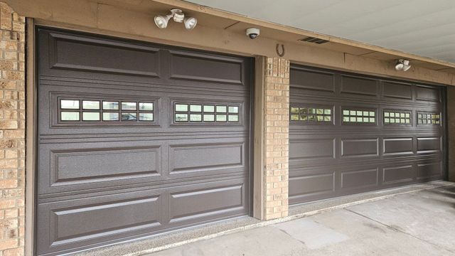 Two dark brown garage doors on a beige house exterior with stone columns and windows.