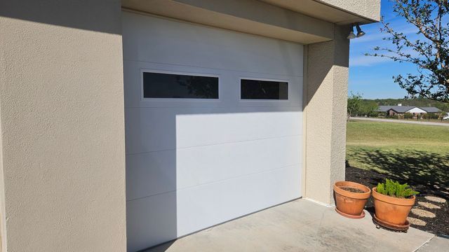 Modern garage with white door, small windows, and potted plants beside a beige house wall