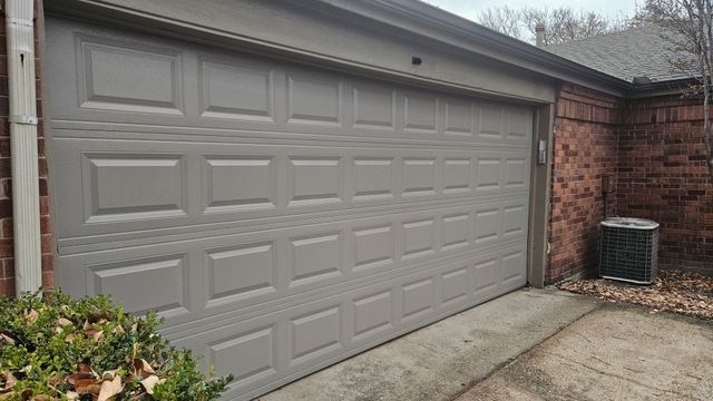 Closed beige garage door beside a brick wall and concrete driveway in a residential setting