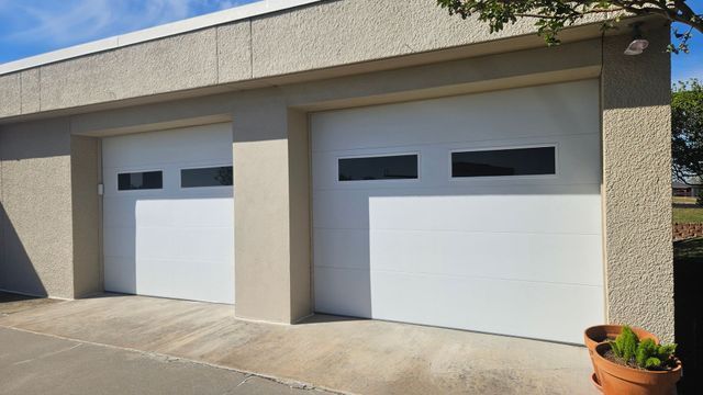 Two white garage doors on a beige house exterior with a concrete driveway and potted plant