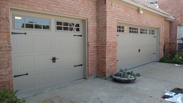 Two gray garage doors on a brick house driveway, with a small planter in front.