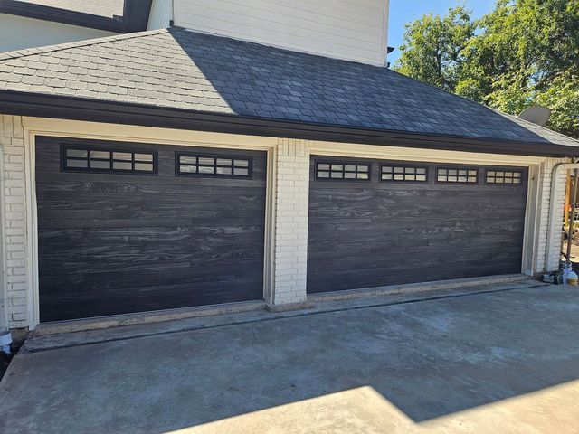Two dark double garage doors on a beige suburban house with a concrete driveway