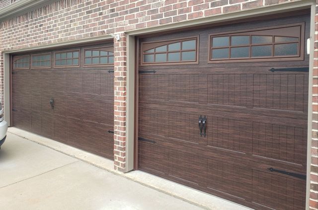 Two brown garage doors on a brick house with small windows above each door