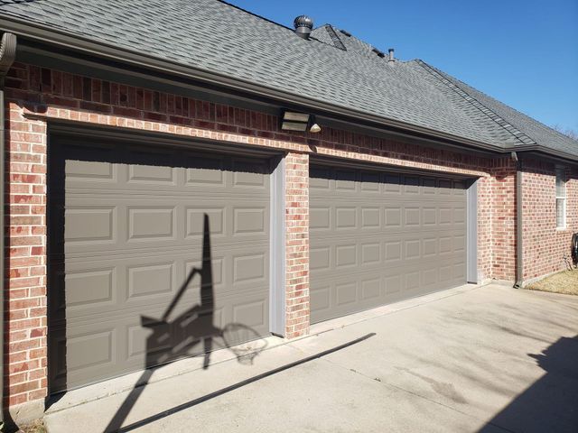 Two tan garage doors on a brick house with sunlight and a shadow across the driveway