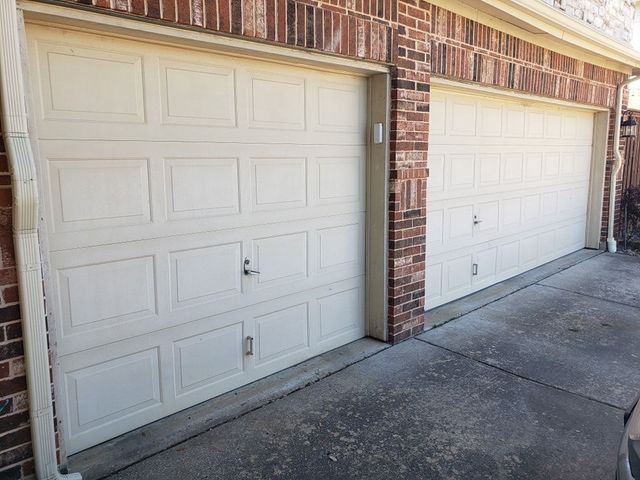 Two white paneled garage doors beside a brick wall and concrete driveway