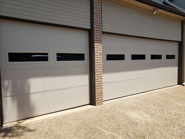 Two beige garage doors with narrow windows beside a brick column on a sunlit driveway