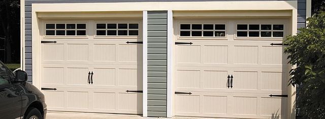 Two white garage doors on a beige house with small windows above each door.