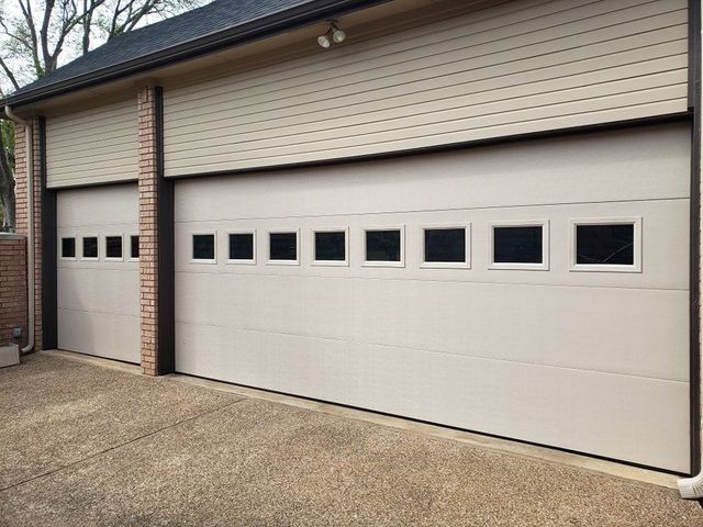 Two beige garage doors with small square windows on a house exterior