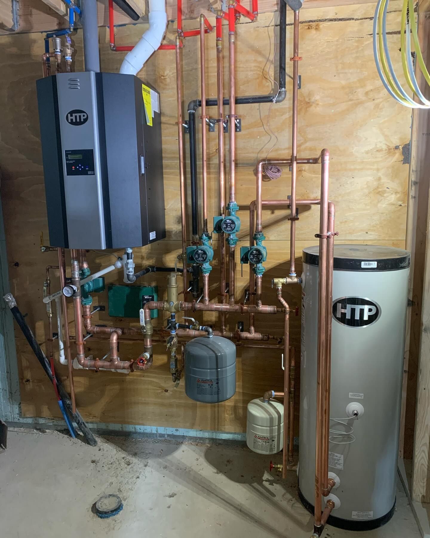 Basement utility room with water heater, boiler, and exposed copper plumbing on plywood wall.