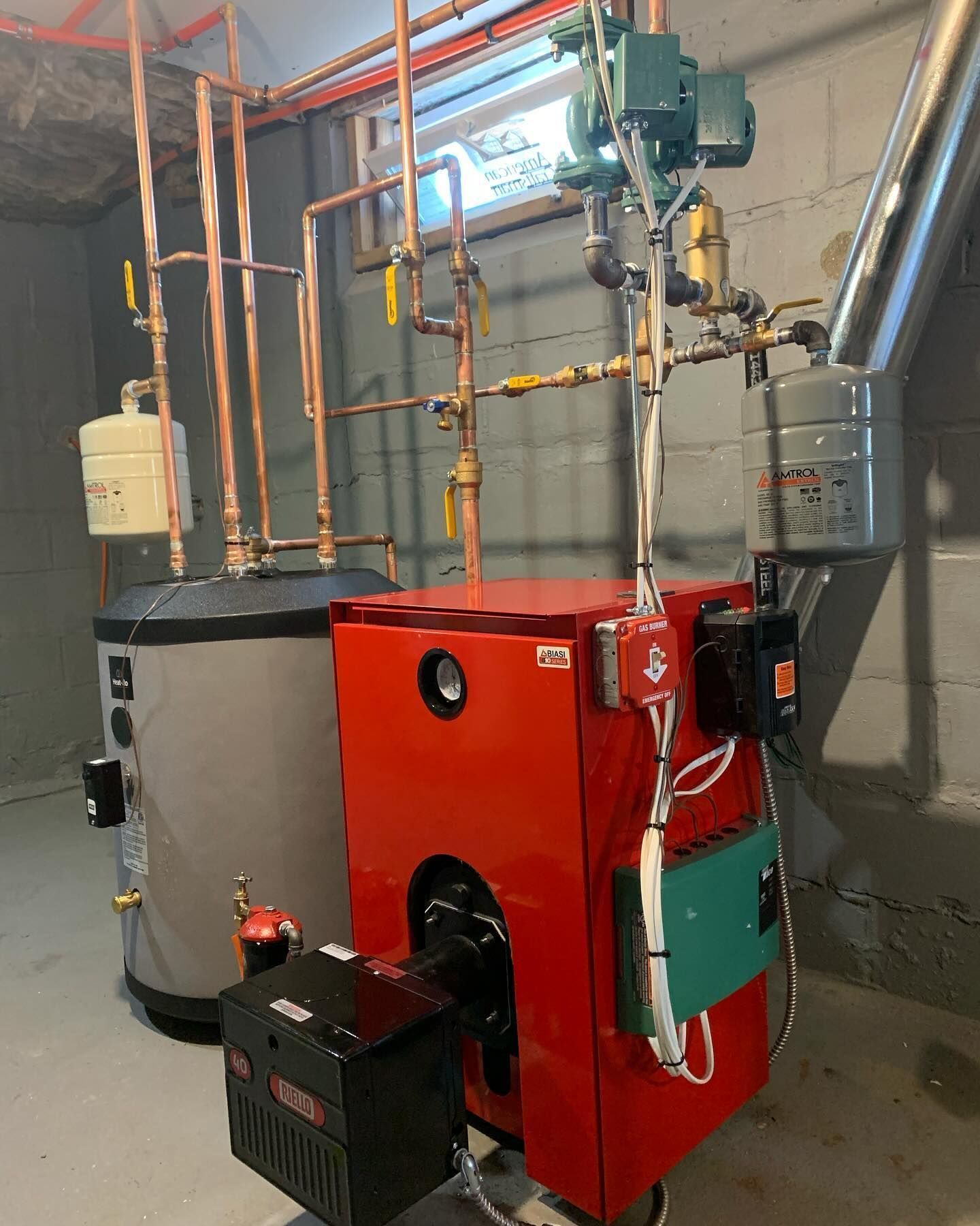 Red industrial boiler with pipes and control panel in a utility room