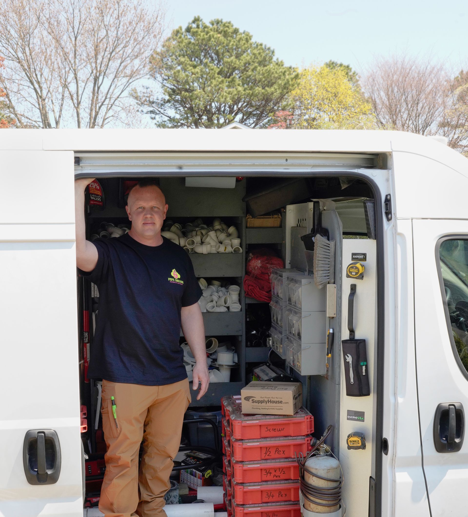 Person standing in an open white van loaded with stacked red crates and supplies outdoors.