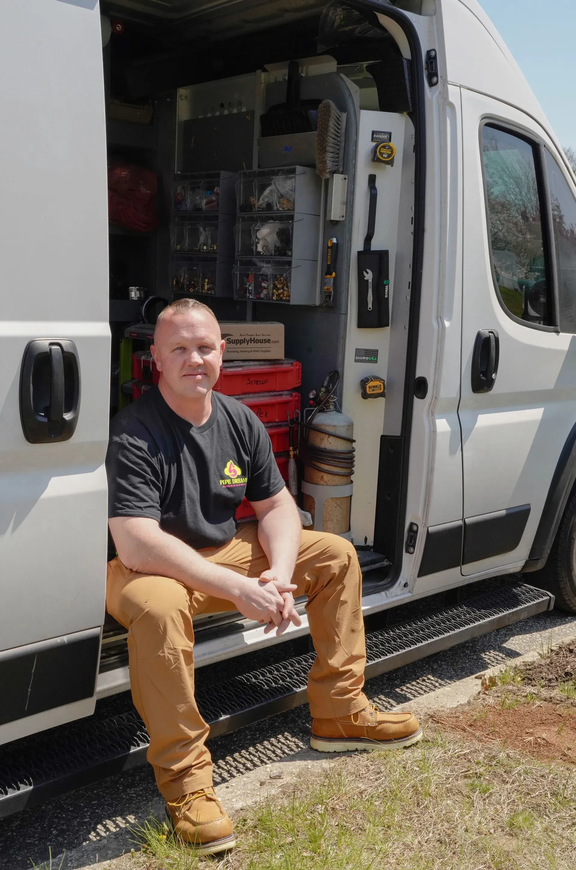 Man sitting on the step of a white van with the side door open, looking at the camera.