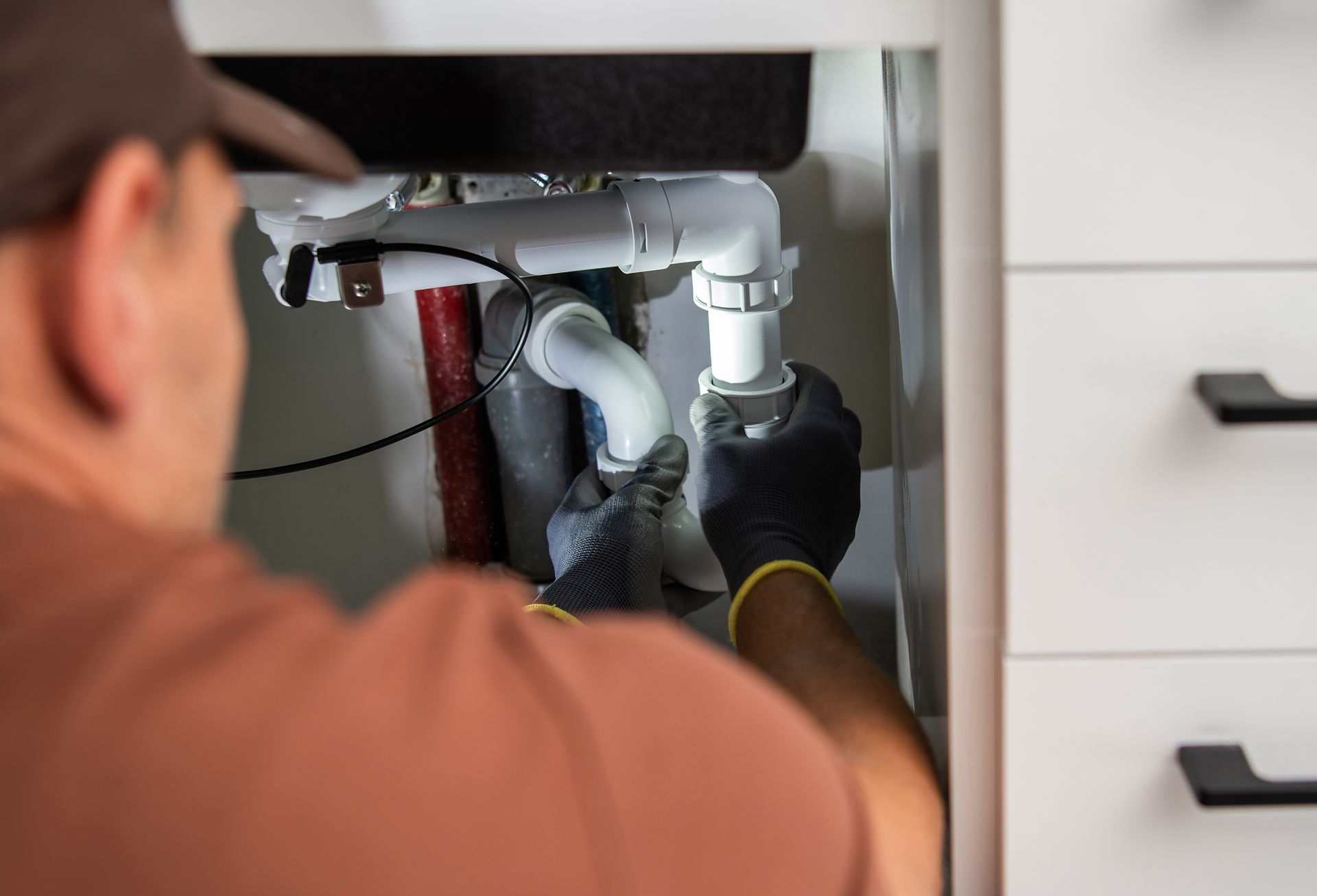 Person repairing plumbing under a sink with a wrench and gloves
