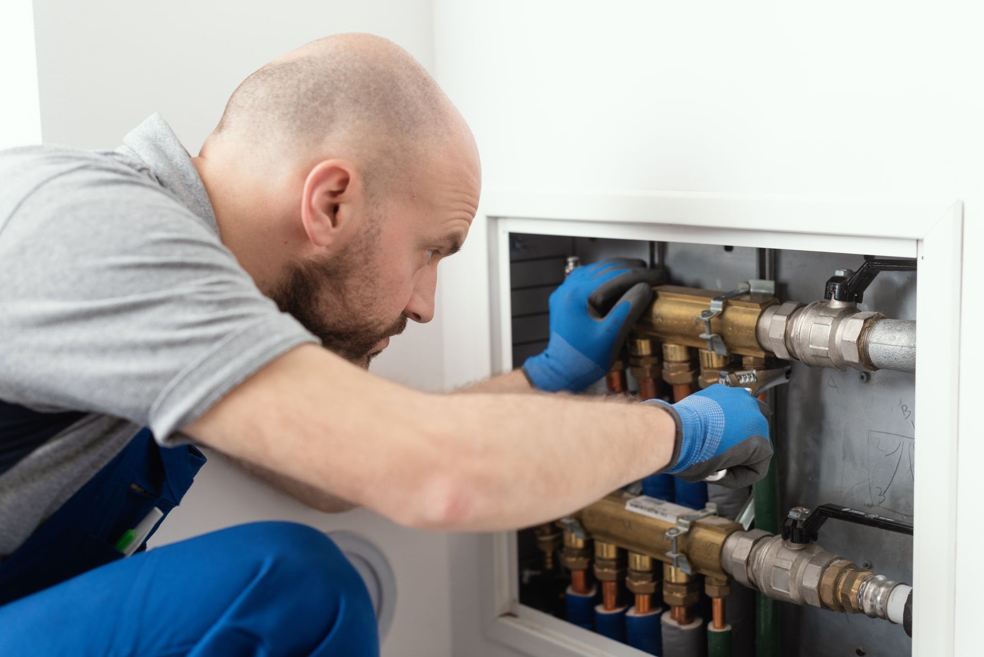 Technician in blue gloves inspecting plumbing pipes inside a wall panel