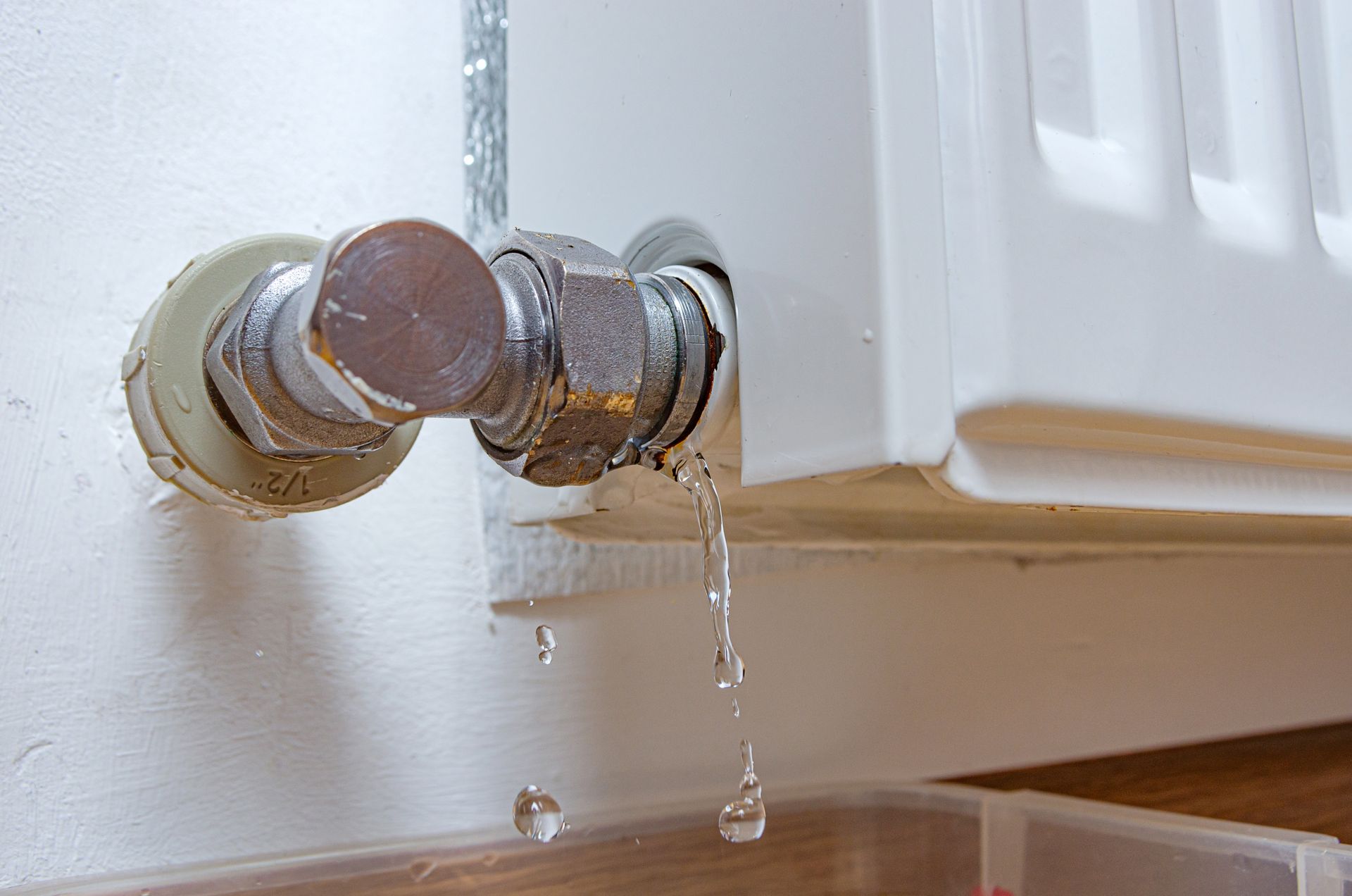 Leaking radiator valve dripping water onto a wooden floor beside a white radiator