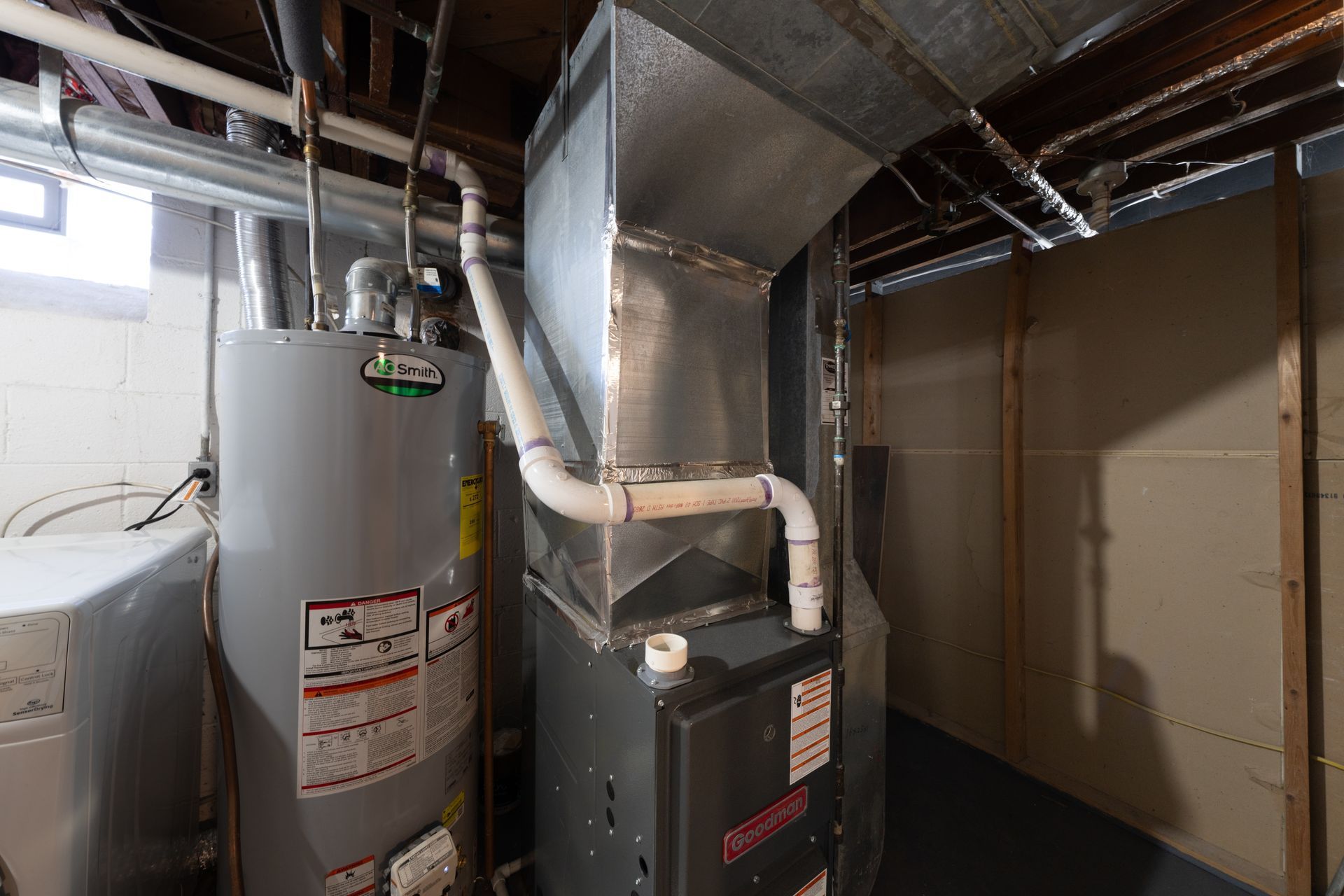 Basement HVAC and water heater with metal ductwork and pipes in a utility room.