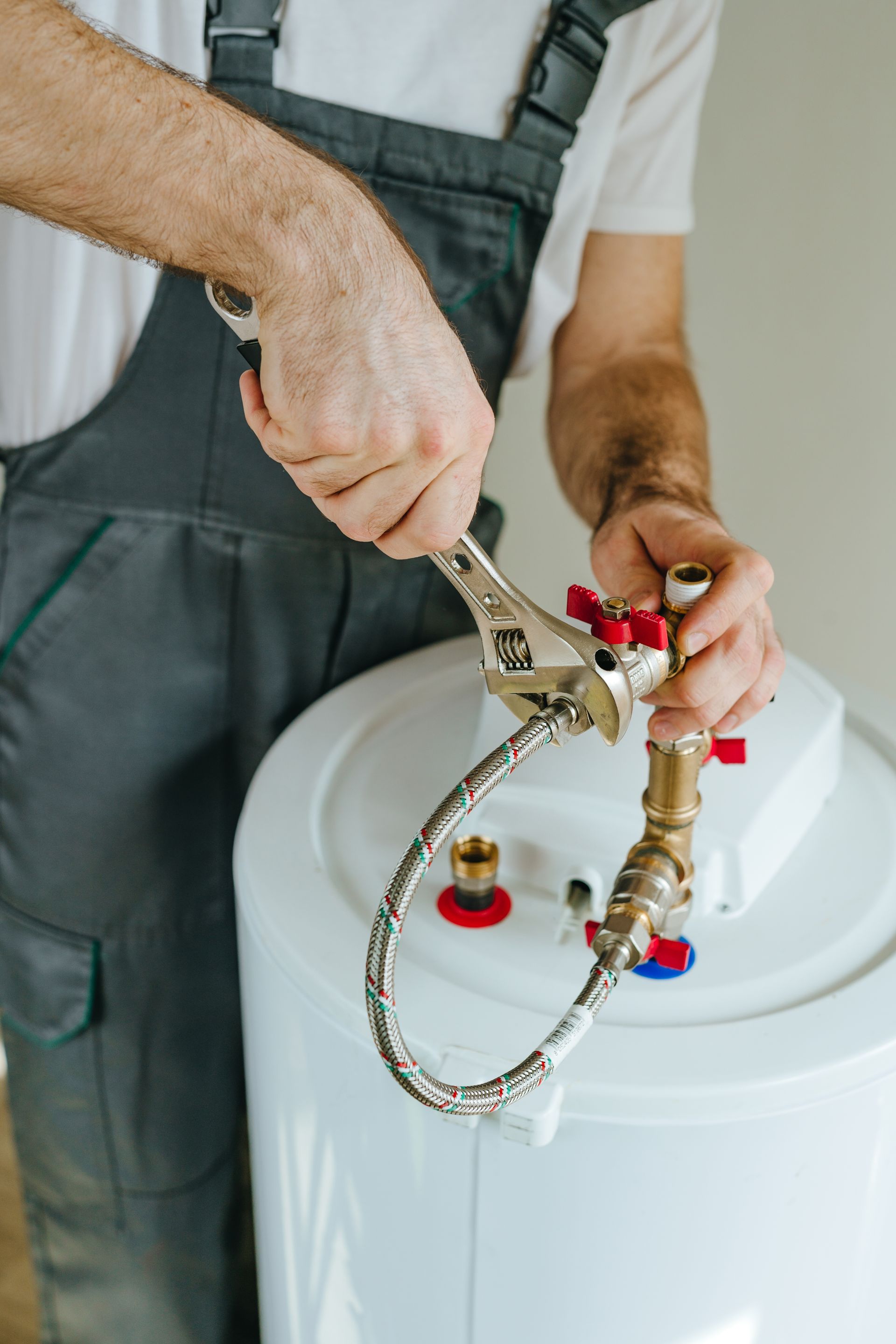 Plumber installing a brass fitting on a white water heater with a wrench