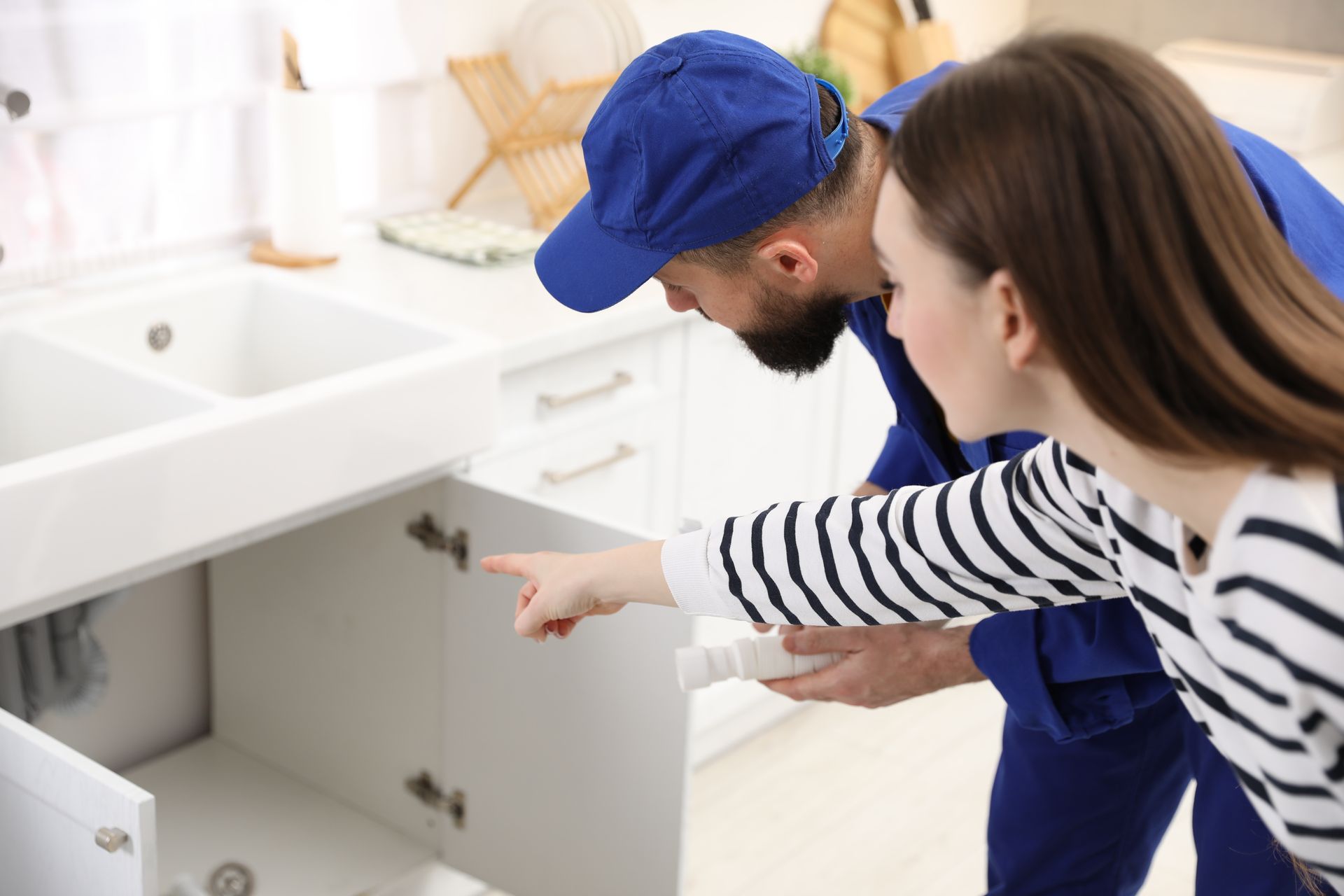 Two people inspecting a sink cabinet under a white bathroom vanity