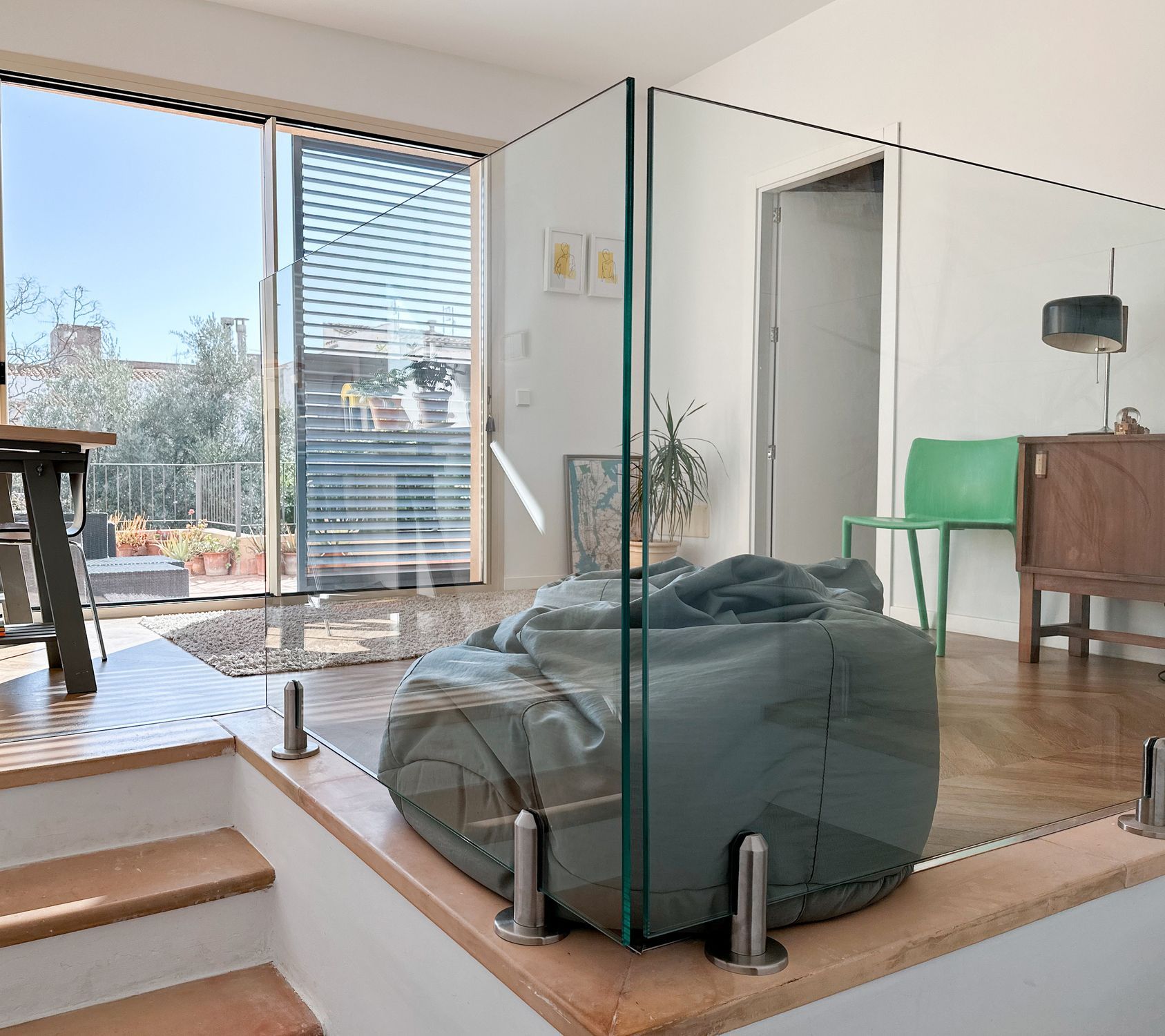 A modern home interior with glass railings, a beanbag, and a view of an outdoor terrace.