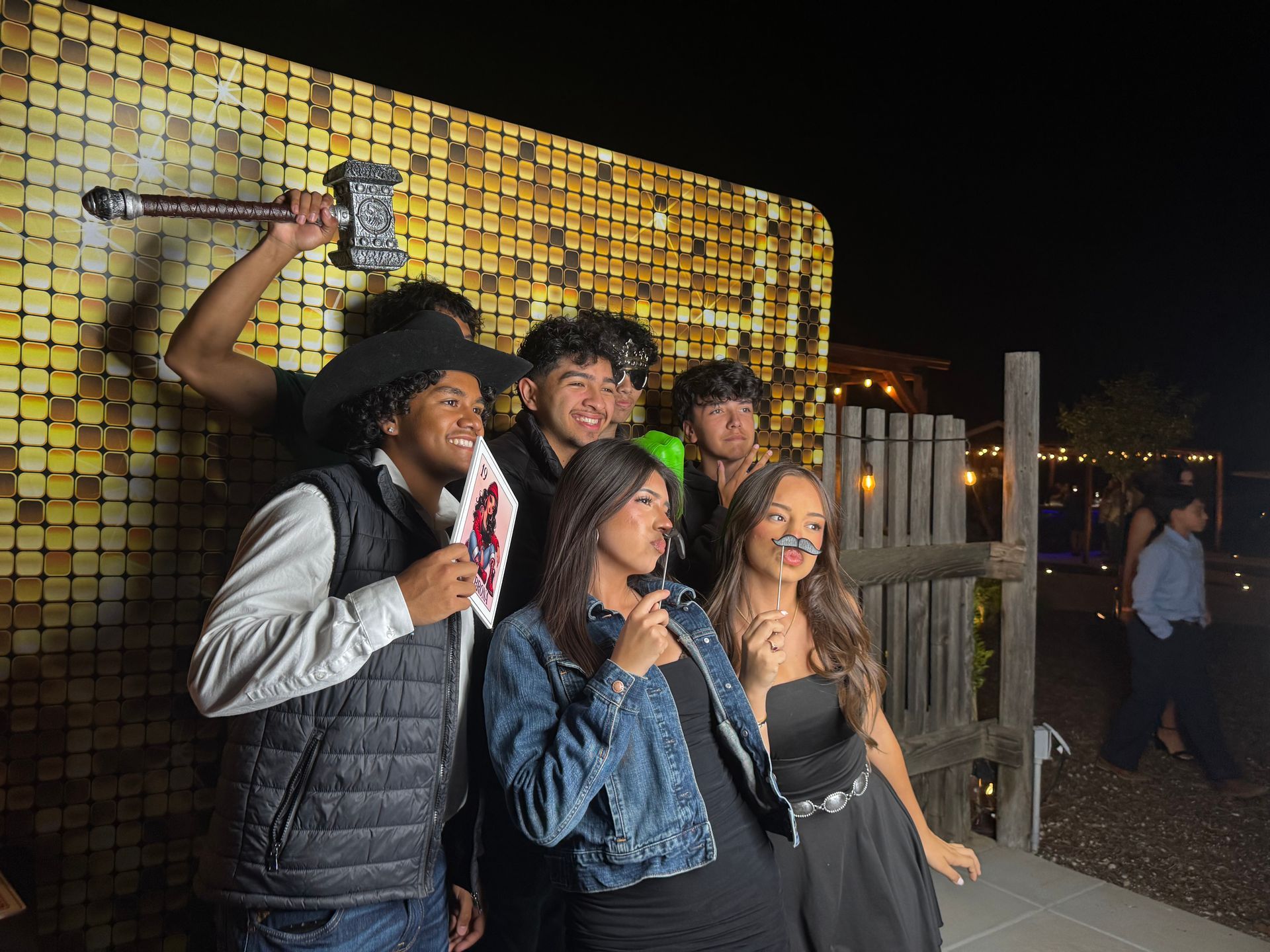 Guests posing at Isabella’s Quinceañera photo booth with a gold backdrop in Perris, CA