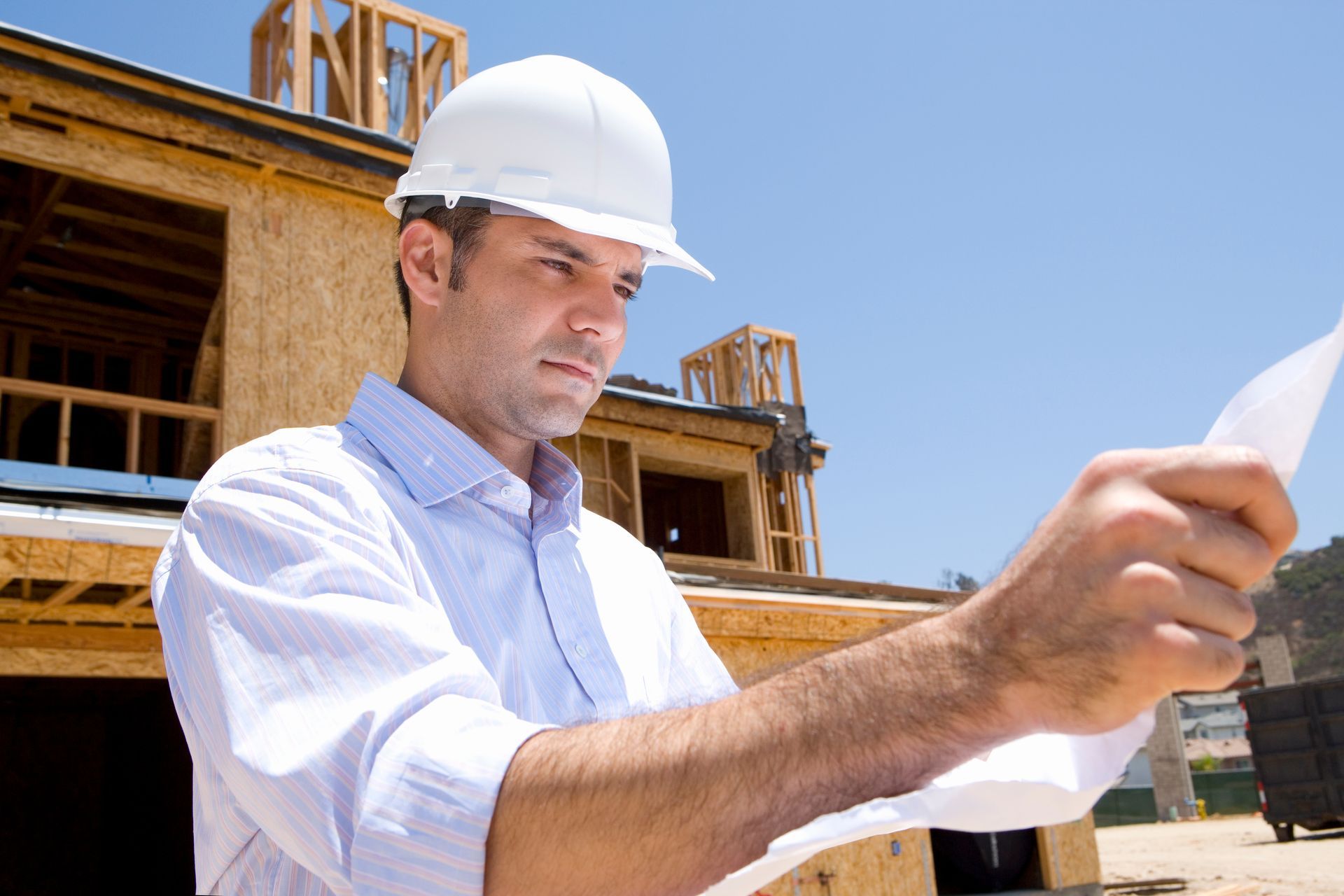 Construction worker in a white hard hat reviewing plans at a building site