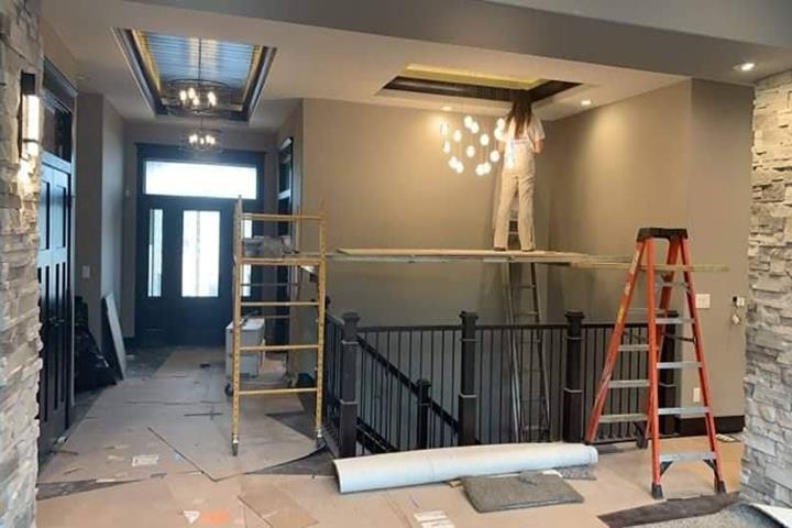 Person painting a ceiling in a hallway. Scaffolding, ladders, and exposed construction materials are present.