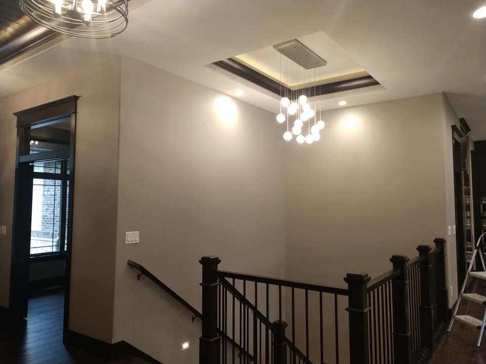 Hallway with stairs and dark wooden railing, beige walls, chandelier, and recessed lighting.