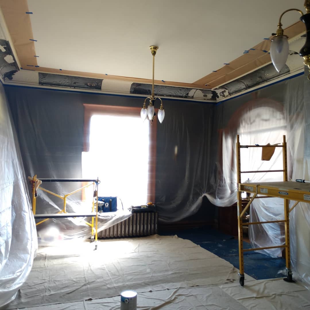 Room under renovation, covered in plastic sheeting. Scaffolding, sunlight through a window, and exposed 