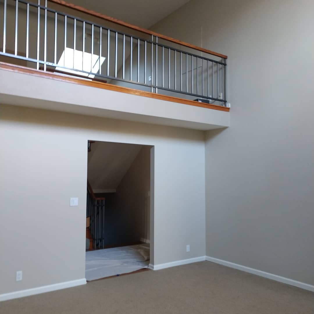 Beige interior with a loft. Metal railing on a wood trim. Open doorway to stairs.