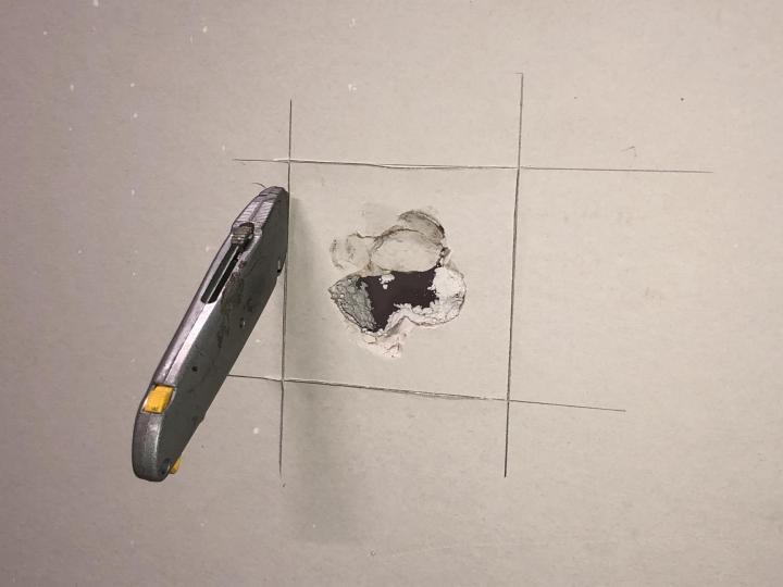 Utility knife next to a damaged wall. A hole is outlined with pencil.